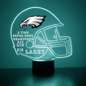 May include: A white and green neon sign shaped like a football helmet with the Philadelphia Eagles logo and the text "2 TIME SUPER BOWL CHAMPIONS LII LIX #10 LARRY".