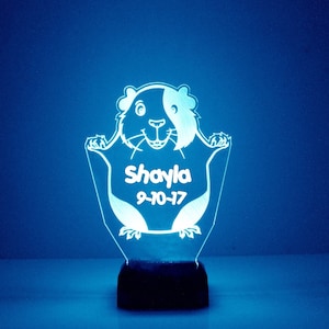 Puede incluir: Una luz nocturna de acrílico blanco con forma de conejillo de indias con el nombre "Shayla" y la fecha "9-10-17" inscritos en ella.