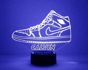 May include: White outline of a high-top sneaker with the name Calvin underneath. The sneaker is on a black base with a blue background.