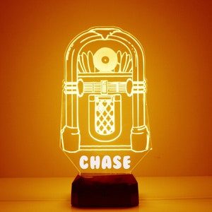May include: A white illuminated jukebox night light with the name "CHASE" on the base. The jukebox is a silhouette with a record on the top and a speaker grill on the front.