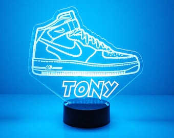 May include: A white 3D printed night light shaped like a sneaker with the word "TONY" underneath. The night light is on a black base and is illuminated with a blue light.