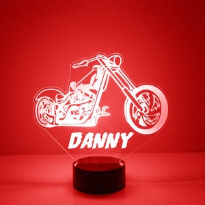 May include: White silhouette of a motorcycle with the name "DANNY" underneath. The motorcycle is on a black base with a red background.
