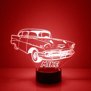 May include: A white silhouette of a classic Chevrolet car with the word "CHEVROLET" on the front, and the name "MIKE" below the car. The car is on a black base with a white light.