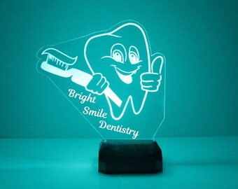 May include: A white acrylic night light shaped like a smiling tooth holding a toothbrush. The light has the text "Bright Smile Dentistry" on it.