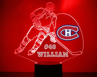 May include: A white hockey player silhouette with a stick and a red and blue Montreal Canadiens logo. The player's number 40 and the name "WILLIAM" are below the logo. The silhouette is on a black base.