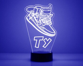 May include: White 3D printed night light shaped like a sneaker with the name "Ty" printed below it. The night light is on a black base and is illuminated with a blue light.