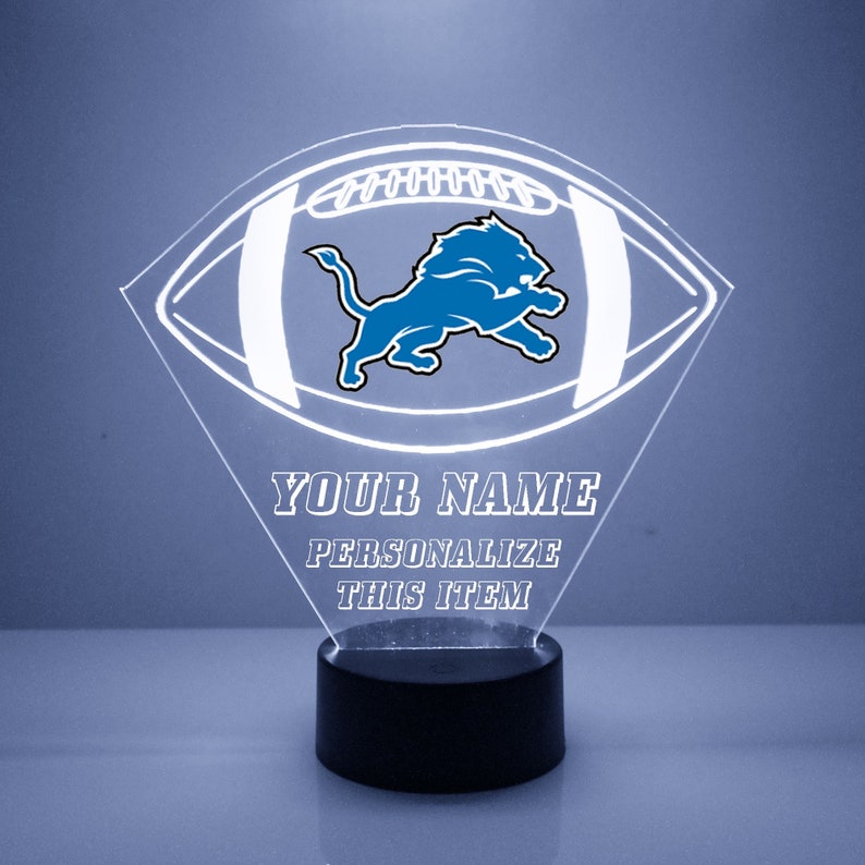 May include: A white acrylic football-shaped night light with a blue Detroit Lions logo. The text "YOUR NAME PERSONALIZE THIS ITEM" is printed below the logo.