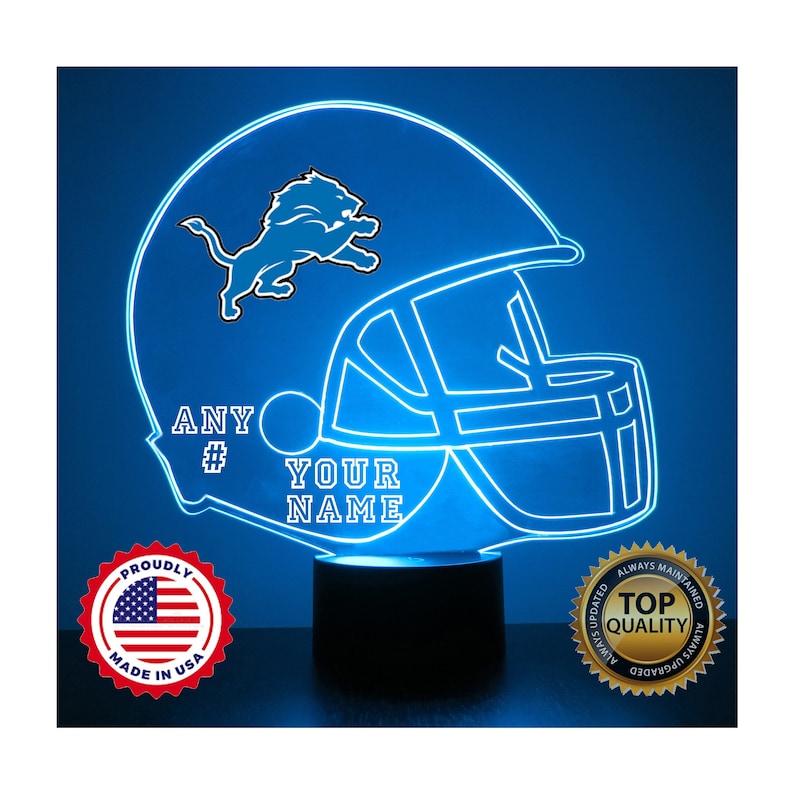 May include: A blue neon light shaped like a football helmet with a Detroit Lions logo and the text "ANY # YOUR NAME". The light is on a black base and has a red, white, and blue sticker that says "Proudly Made in USA".