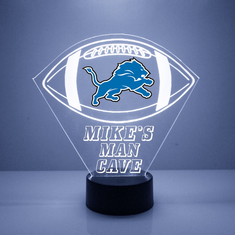 May include: A white illuminated acrylic football with a blue Detroit Lions logo and the text "MIKE'S MAN CAVE" on a black base.