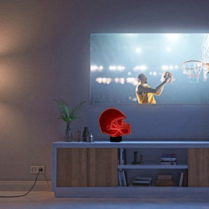 May include: A red and black football helmet night light on a wooden shelf in front of a television screen showing a basketball game.