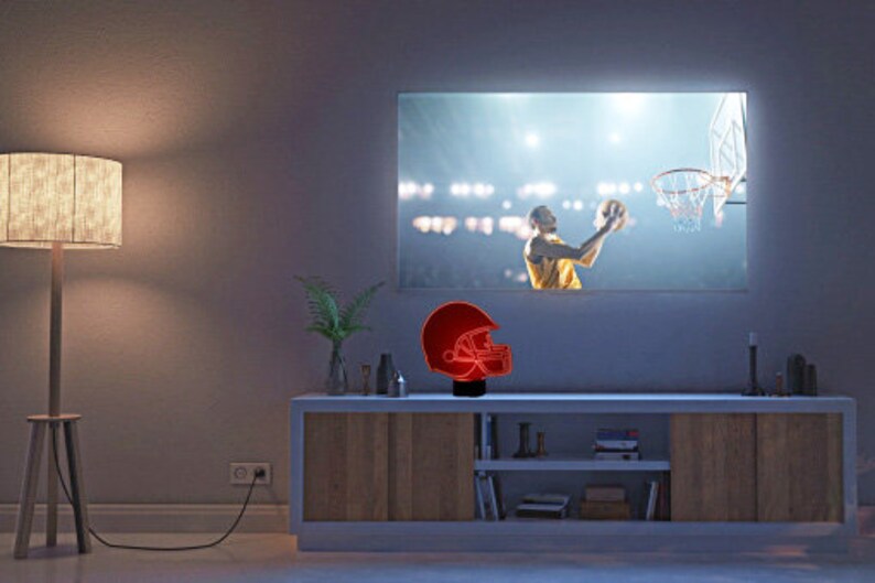 May include: A red and black football helmet night light on a wooden shelf in front of a television screen showing a basketball game.