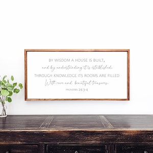 May include: A wooden sign with a white background and a brown frame. The sign features a quote from Proverbs 24:3-4, which reads: "By wisdom a house is built, and by understanding it is established. Through knowledge its rooms are filled with rare and beautiful treasures."