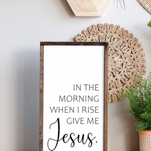 May include: A wooden sign with a white background and brown frame. The sign has black text that reads "In the morning when I rise give me Jesus."