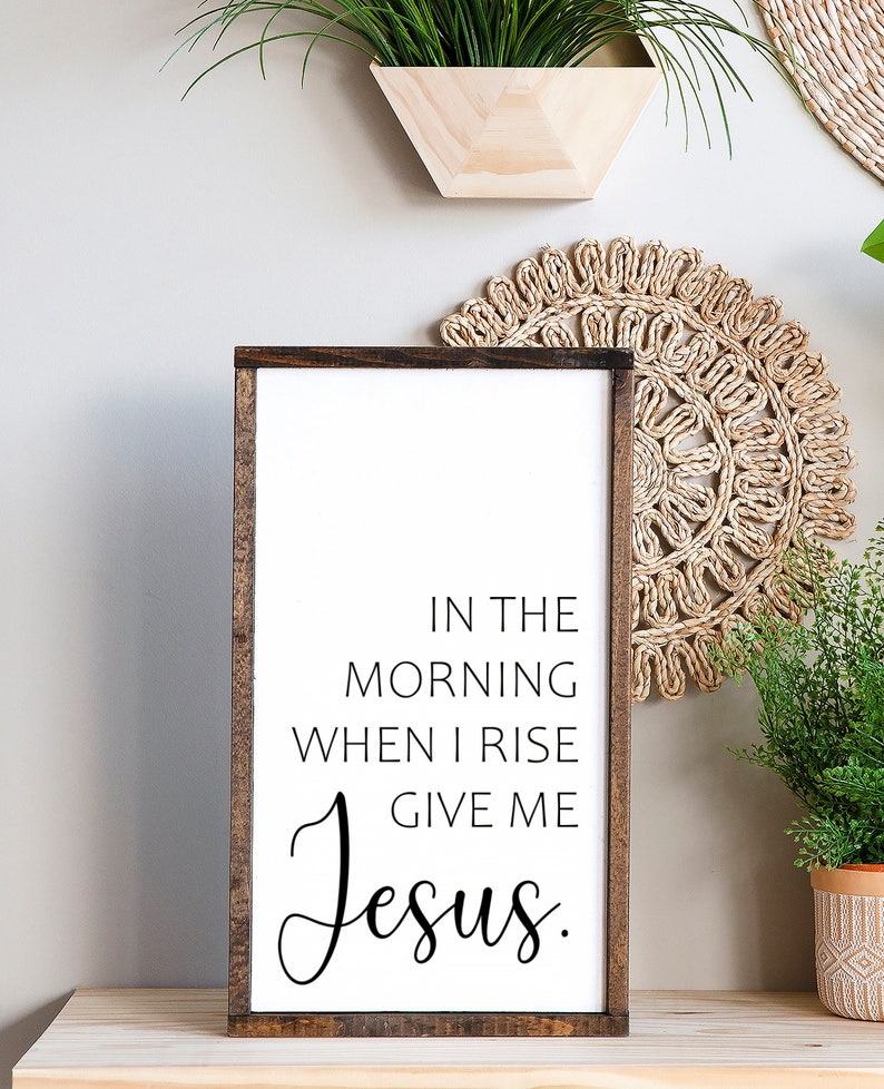 May include: A wooden sign with a white background and brown frame. The sign has black text that reads "In the morning when I rise give me Jesus."