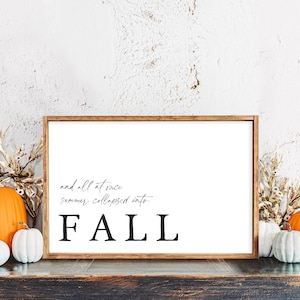 May include: A framed sign with the word "FALL" in large, bold letters. The sign is surrounded by pumpkins in various sizes and colors, and dried wheat stalks. The text on the sign reads "and all at once summer collapsed into".