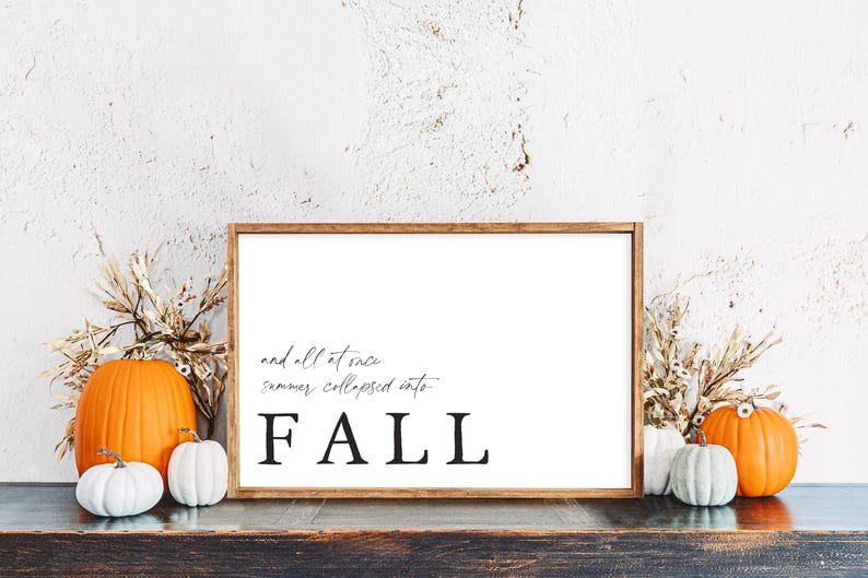 May include: A framed sign with the word "FALL" in large, bold letters. The sign is surrounded by pumpkins in various sizes and colors, and dried wheat stalks. The text on the sign reads "and all at once summer collapsed into".