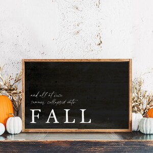 May include: A black framed sign with the word "FALL" in white, along with the phrase "and all at once summer collapsed into". The sign is surrounded by pumpkins and dried foliage, creating a fall theme.