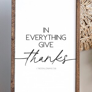 Op de afbeelding: Een wit ingelijst bord met de tekst "IN EVERYTHING GIVE thanks" en de bijbelverwijzing "1 Thessalonicenzen 5:18".