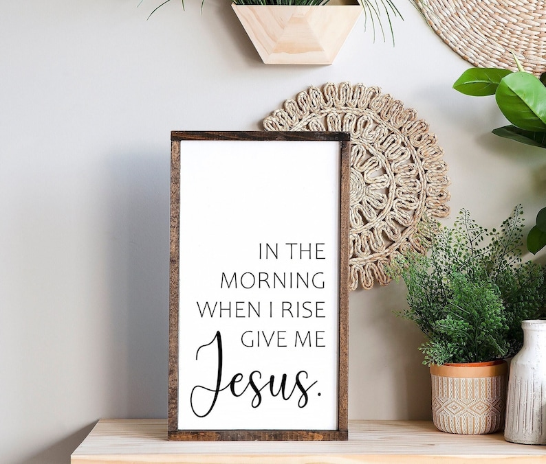May include: A wooden sign with the text "In the morning when I rise give me Jesus." The sign is white with black lettering and has a brown wooden frame.