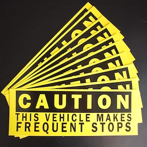 以下が含まれることがあります： 「CAUTION THIS VEHICLE MAKES FREQUENT STOPS」と書かれた黄色と黒の注意喚起サインの束。