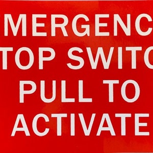 May include: Red sign with white text that reads "EMERGENCY STOP SWITCH PULL TO ACTIVATE"
