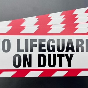 Peut inclure: Un panneau rouge et blanc rayé avec le texte "NO LIFEGUARD ON DUTY" en lettres noires.
