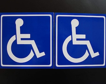 May include: Two blue and white handicap accessible signs. Each sign features the international symbol of access, a stylized person in a wheelchair, in white against a blue background. The signs are square with a white border.