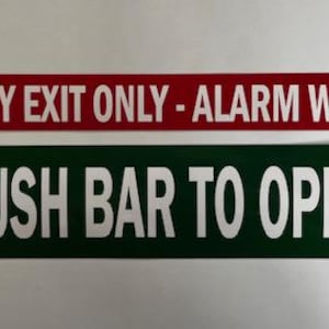 May include: Two rectangular signs with white text on a red and green background. The red sign reads "EMERGENCY EXIT ONLY - ALARM WILL SOUND." The green sign reads "PUSH BAR TO OPEN."