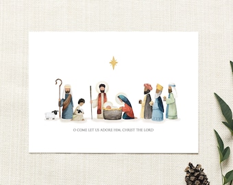 May include: A white rectangular card featuring a watercolor illustration of a nativity scene with figures, a sheep, and a gold star above. The text O COME LET US ADORE HIM, CHRIST THE LORD is printed in black below the figures on the white background.