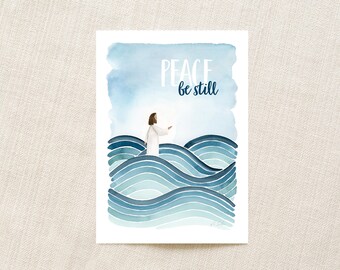May include: A rectangular art print featuring a watercolour illustration of a figure in a white robe standing amidst stylised blue ocean waves. The text PEACE be still is printed in white and dark blue at the top against a light blue sky background.