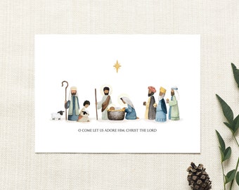 May include: A rectangular greeting card featuring a watercolor illustration of a nativity scene with figures, a sheep, and a gold star above. The text O COME LET US ADORE HIM, CHRIST THE LORD is printed in black at the bottom center of the white card.