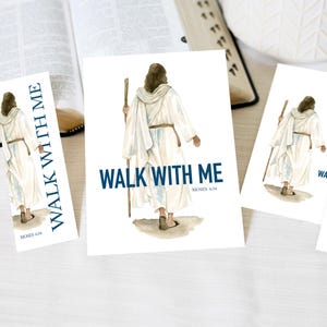 May include: A set of paper prints and bookmarks featuring a watercolor illustration of a figure in a white robe walking away while holding a wooden staff. The text "WALK WITH ME" and "MOSES 6:34" is printed in dark blue on each of the paper items.