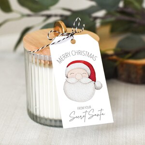 May include: White gift tag with a cartoon Santa Claus illustration. The tag says "Merry Christmas" and "From your Secret Santa".