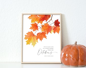 May include: A framed wall art print featuring a watercolor illustration of vibrant orange, red, and yellow maple leaves on a branch. The text reads: I'm so glad I live in a world where there are Octobers, followed by Anne of Green Gables.