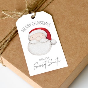 May include: White gift tag with a watercolor illustration of Santa Claus's face. The tag says "Merry Christmas" and "From your Secret Santa".