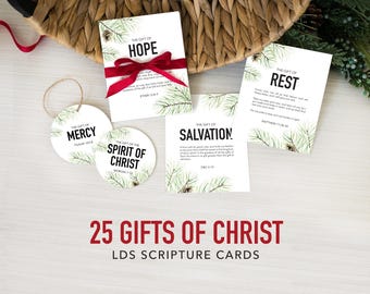 May include: A set of white rectangular and circular cards featuring green pine branch illustrations and black text including The Gift of Hope, Rest, Mercy, Spirit of Christ, and Salvation. A red ribbon is tied around one card. Text reads 25 Gifts of Christ LDS Scripture Cards.