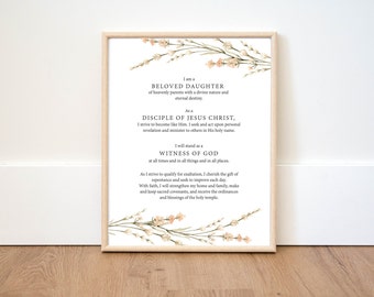 Könnte beinhalten: Ein gerahmter Kunstdruck mit schwarzem Text auf weißem Hintergrund, verziert mit aquarellartigen pfirsichfarbenen und grünen Blumenranken oben und unten. Der Text lautet: I am a BELOVED DAUGHTER, DISCIPLE OF JESUS CHRIST, WITNESS OF GOD.