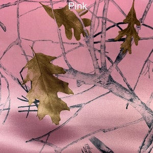 May include: Pink camouflage fabric with a pattern of tree branches and leaves. The fabric has the text "True Timber Snowfall Pink" printed on it. The leaves are a golden brown color.