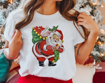 Op de afbeelding: Wit T-shirt met een vintage illustratie van Sinterklaas die een zak met cadeaus draagt. De illustratie is in cartoon-stijl en toont Sinterklaas met een rood pak, witte baard en een vrolijke uitdrukking. De tekst "Merry Christmas" staat op de zak.