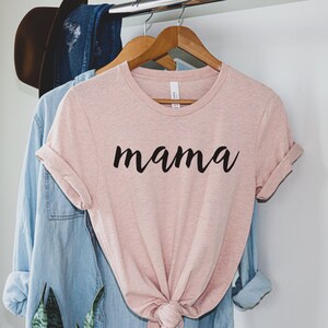 Może przedstawiać: R&oacute;żowy t-shirt z napisem "mama" napisanym czarnym, ozdobnym pismem.