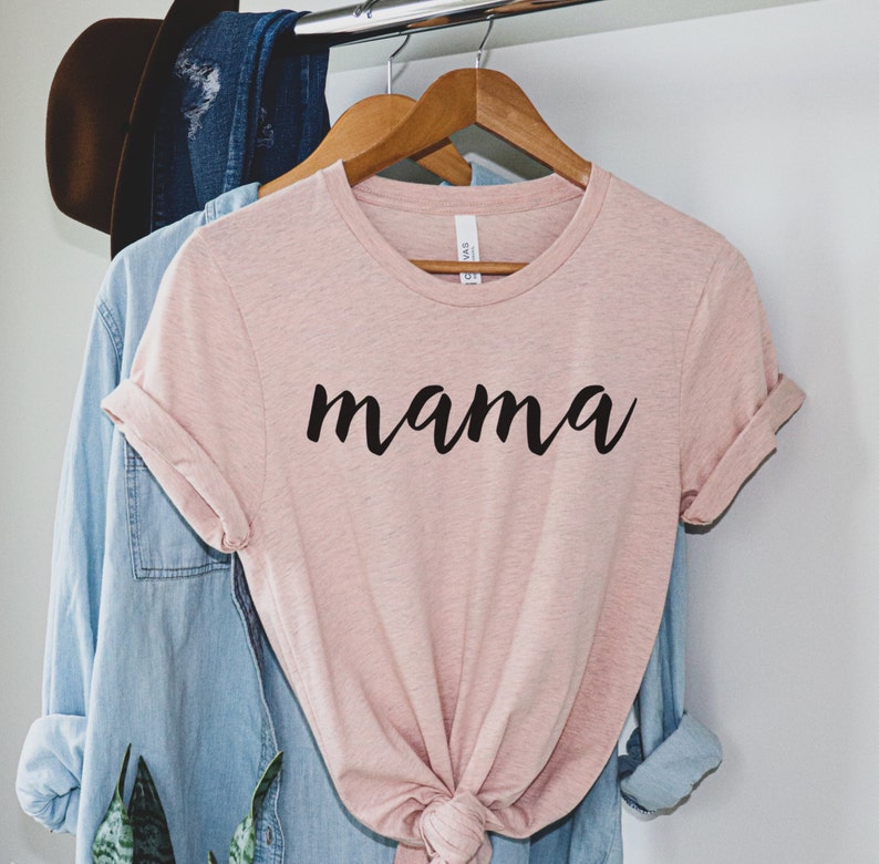Może przedstawiać: R&oacute;żowy t-shirt z napisem "mama" napisanym czarnym, ozdobnym pismem.
