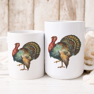Puede incluir: Dos tazas de cer&aacute;mica blanca con una ilustraci&oacute;n colorida de un pavo en cada una. El pavo tiene la cabeza roja, plumas verdes y marrones y un pico amarillo.