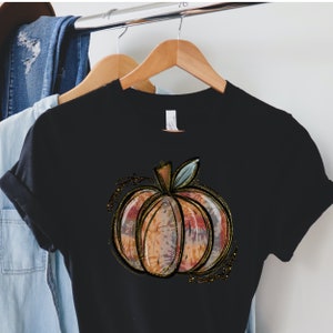 May include: Black t-shirt with a gold glitter pumpkin design. The pumpkin is a watercolor style with orange, pink, and blue colors.