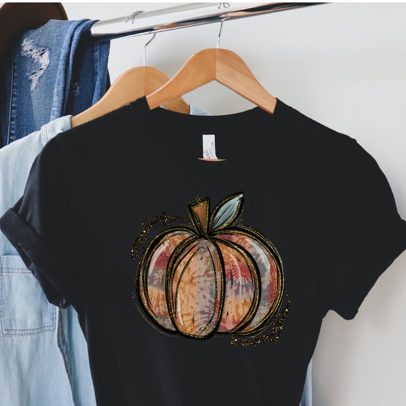 May include: Black t-shirt with a gold glitter pumpkin design. The pumpkin is a watercolor style with orange, pink, and blue colors.
