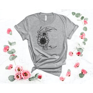 May include: A gray t-shirt with a black graphic of a crescent moon with sunflowers and leaves around it.
