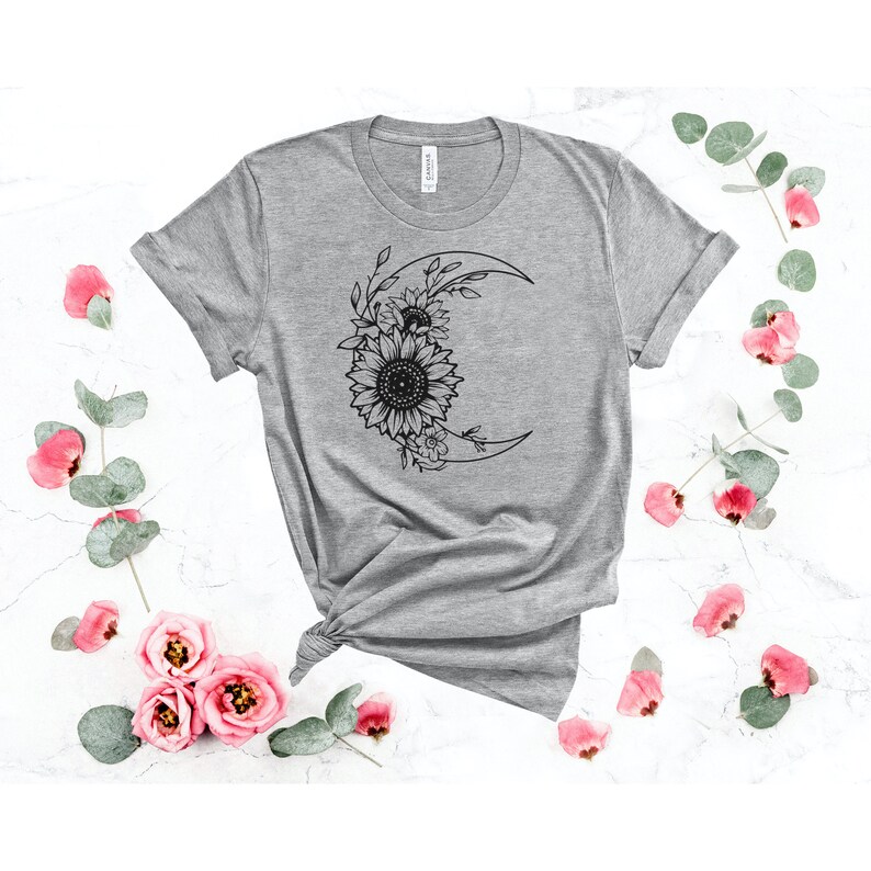 May include: A gray t-shirt with a black graphic of a crescent moon with sunflowers and leaves around it.