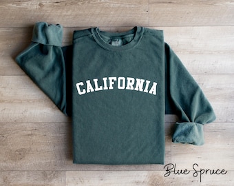 Peut inclure: Un sweat-shirt vert foncé avec le mot "CALIFORNIA" imprimé en blanc sur le devant. Le sweat-shirt a un aspect vieilli et est fait d'un tissu doux et confortable.