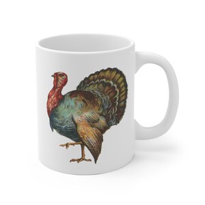 Puede incluir: Taza de caf&eacute; de cer&aacute;mica blanca con una ilustraci&oacute;n colorida de un pavo. El pavo tiene la cabeza roja, plumas azules y verdes y plumas de cola marrones y doradas.