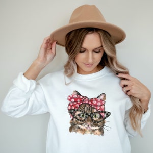 Può includere: Felpa bianca con una grafica di un gatto che indossa una fascia rossa a pois e occhiali.