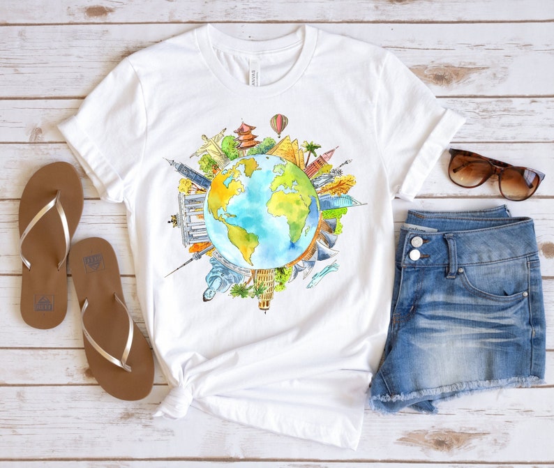 May include: White t-shirt with a watercolor illustration of the Earth surrounded by famous landmarks from around the world. The landmarks include the Eiffel Tower, the Statue of Liberty, the Great Wall of China, and the Taj Mahal.
